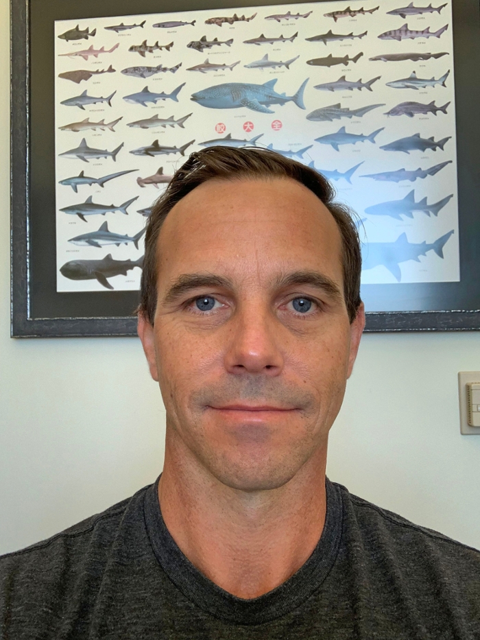 Wells poses against a poster of some of the marine animals he's dedicated his life to studying, sharks. 